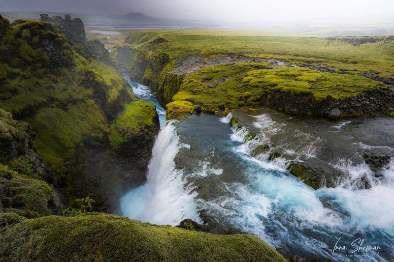 A turquoise river plunging into a narrow mossy canyon under low mist