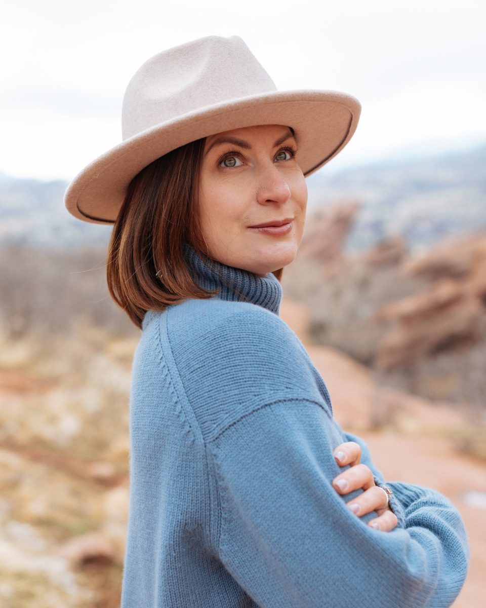 Inna Sherman in a wide-brimmed hat and blue sweater at Red Rocks, Colorado, looking back over her shoulder