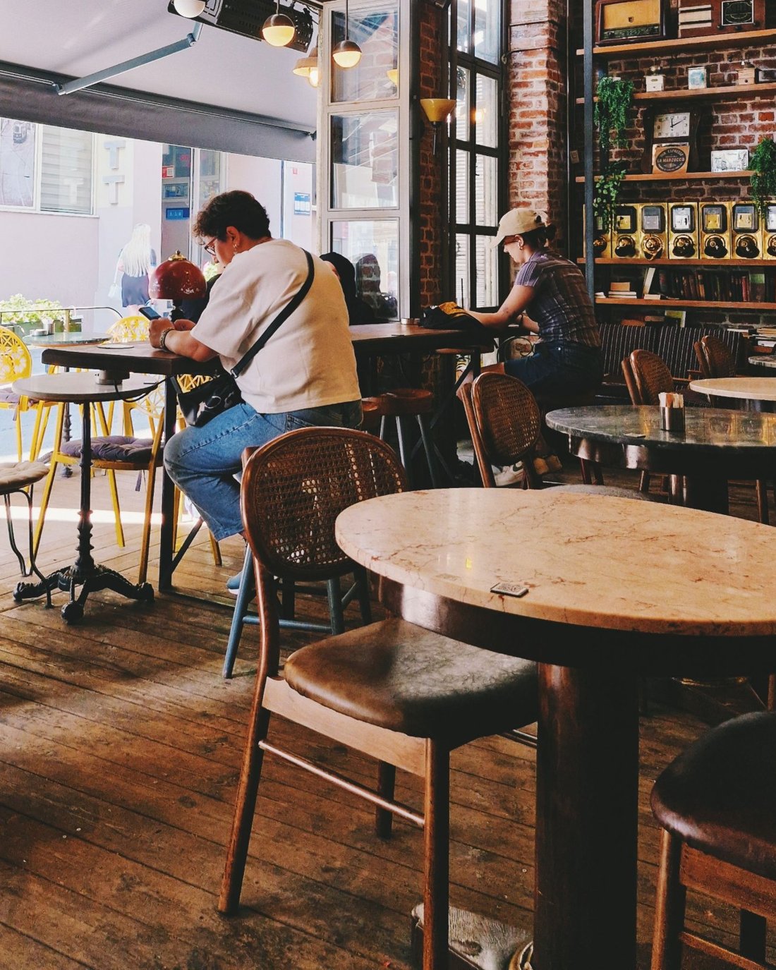 A sunlit coffee shop with marble tables, cane chairs, brick walls and shelves of coffee grinders